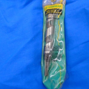Puede incluir: Un paquete verde y amarillo que contiene una broca Greenlee Nail Eater II de 1/4 de pulgada. El paquete tiene el texto "Greenlee Nail Eater II 1/4 inch Power Bits" e "Inches Courtes" impreso en &eacute;l.