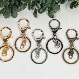 May include: Five keyrings with different finishes: gold, silver, and bronze. Each keyring has a round ring and a lobster claw clasp.