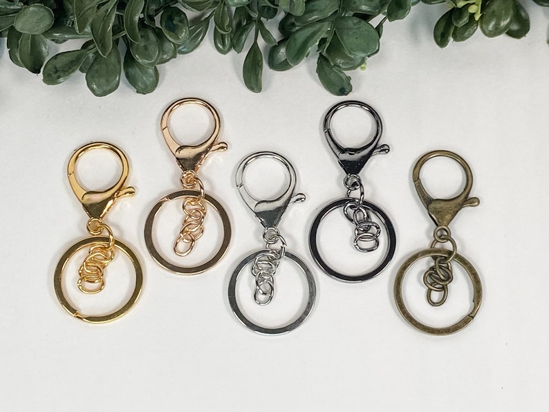 May include: Five keyrings with different finishes: gold, silver, and bronze. Each keyring has a round ring and a lobster claw clasp.