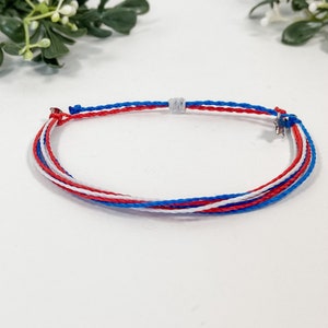May include: A red, white, and blue braided friendship bracelet with a silver star charm.