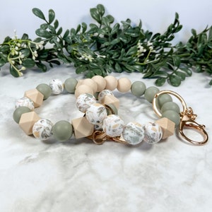 May include: A green and beige silicone beaded keyring with a floral pattern. The keyring has a gold metal clasp.