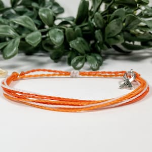May include: Orange and white string bracelet with a silver charm that says "HOPE" in the shape of a ribbon.