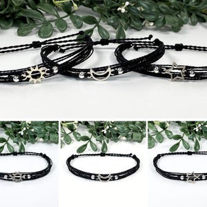 May include: Three black string bracelets with silver charms. The charms are a sun, a crescent moon, and a star.