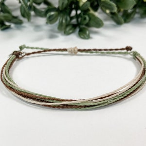 May include: A multi-strand bracelet with brown, green, and white string. The bracelet is tied with a knot at the end.