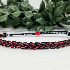 May include: A black and red braided bracelet with a simple knot closure.