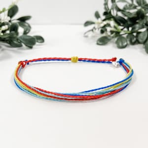 May include: A multi-colored string bracelet with red, blue, yellow, and light blue threads. The bracelet has a silver clasp.