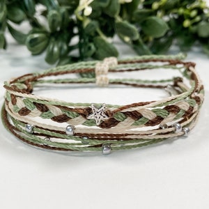 May include: A multi-strand bracelet with a braided design in brown, green, and white threads. The bracelet has silver beads and a silver star charm.