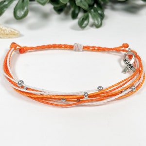 May include: Orange and white friendship bracelet with silver beads and a silver charm that says "HOPE" in all caps.