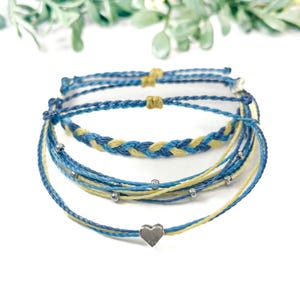 May include: A set of four friendship bracelets in blue and yellow with silver beads and a silver heart charm.