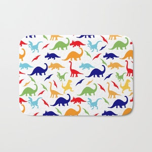 May include: A white bath mat with a colorful dinosaur pattern. The dinosaurs are in various colors, including red, orange, yellow, green, blue, and purple. The dinosaurs are all different sizes and shapes.