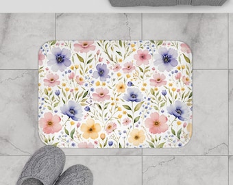 May include: A rectangular bath mat with a floral pattern. The mat features watercolor-style flowers in shades of pink, blue, and yellow, set against a white background. The mat measures 24" x 17".
