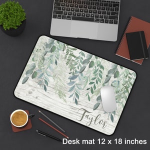 May include: A white wood desk mat with a green leafy design and the name "Taylor" printed in black. The mat measures 12 x 18 inches.