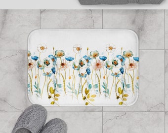 May include: White bath mat with a watercolor floral design featuring blue and pink flowers. The mat measures 24 inches by 17 inches.