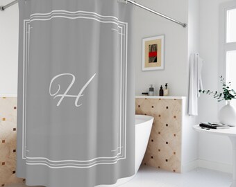 May include: A gray shower curtain with a white border and a white letter "H" in the center. The shower curtain is hanging in a bathroom with a white tub and a tiled wall.