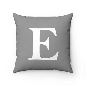 May include: A gray throw pillow with a white letter E in the center.