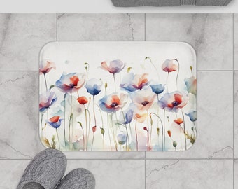 May include: A white bath mat with a watercolor floral design featuring pink, blue, and red flowers. The mat measures 24 inches by 17 inches.