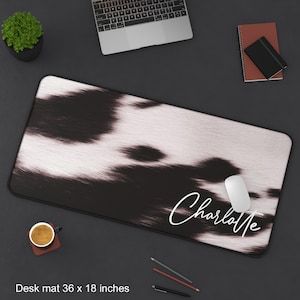 May include: Black and white cowhide patterned desk mat with the name "Charlotte" written in white script. The mat measures 36 x 18 inches.