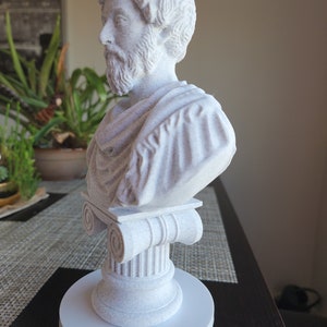 Puede incluir: Busto de escultura blanca de un hombre con barba, vistiendo una toga, sobre un pedestal blanco con una base de columna.
