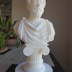 Puede incluir: Busto de escultura blanca de un hombre con barba, vistiendo una toga, sobre un pedestal blanco con una base de columna.