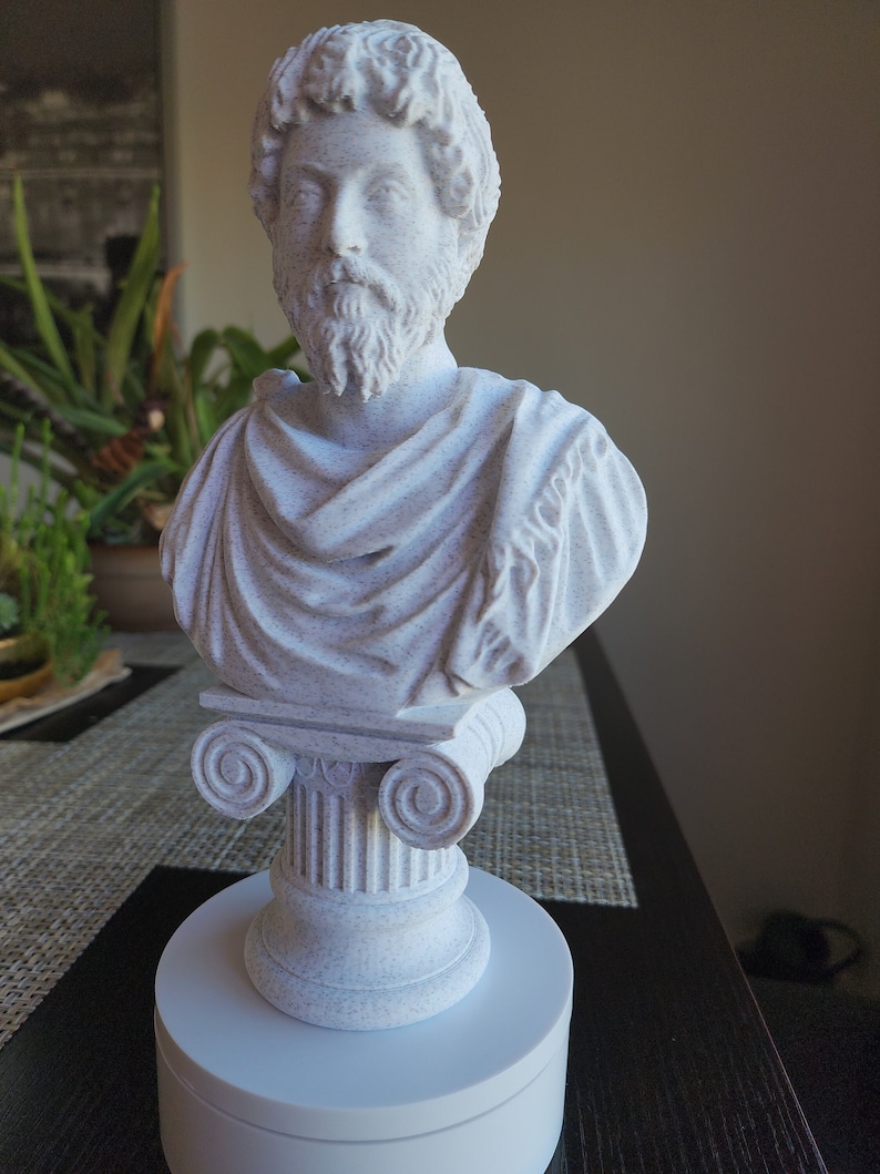 Puede incluir: Busto de escultura blanca de un hombre con barba, vistiendo una toga, sobre una base de columna blanca. La escultura est&aacute; sobre una base circular blanca.