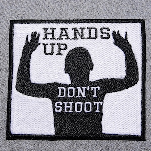 May include: White patch with black border, featuring a black silhouette of a person with arms raised, and the text "HANDS UP DON'T SHOOT" in white.