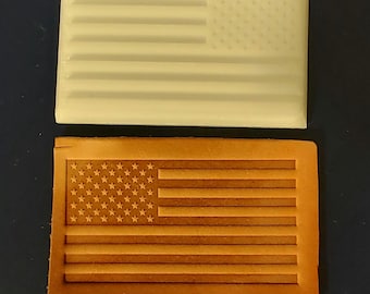 May include: Two rectangular objects, one cream-colored and the other brown, each feature an embossed American flag design. The cream-colored object is smooth, while the brown object appears to be made of leather. The flag design includes stars and stripes.
