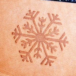 May include: A brown leather patch with a detailed snowflake design embossed into the surface.
