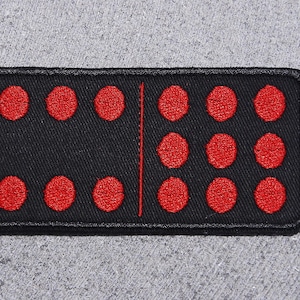 May include: A black fabric patch with a white line down the middle. On each side of the line are red embroidered dots. There are three dots on one side and six dots on the other side.