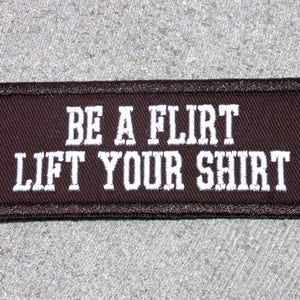 May include: Brown fabric patch with white embroidered text that reads "BE A FLIRT LIFT YOUR SHIRT".