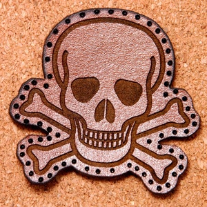 May include: A brown leather skull and crossbones patch with black stitching and black dots around the edges.