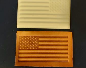 May include: Two rectangular objects, one white and one brown, each featuring the design of the American flag. The white object appears to be made of plastic, while the brown object is made of leather. The flag design includes stars and stripes.