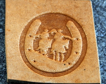 May include: A brown leather patch with a raised design of a horseshoe with two figures inside. The figures are stylized and appear to be dancing.