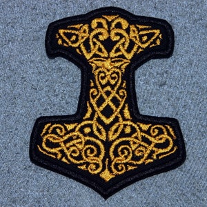 May include: A black and gold embroidered patch featuring a stylized Mjolnir, the hammer of Thor, with intricate knotwork designs.