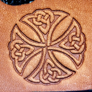 May include: A brown leather surface with a detailed Celtic knot design embossed into the surface. The design is a circular pattern with a cross in the center.