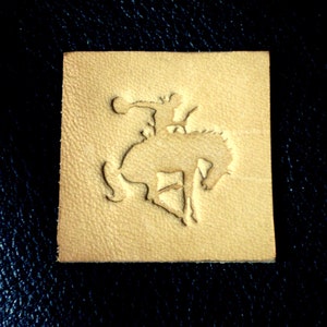 May include: A tan leather patch with a raised design of a cowboy riding a bucking horse.
