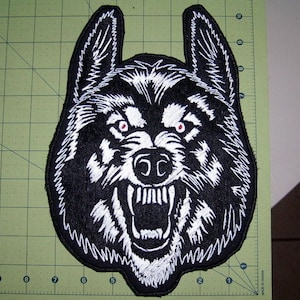 May include: Black and white embroidered patch of a wolf's head with red eyes. The wolf is snarling with its teeth bared.