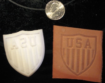 May include: Two close-up images of a shield-shaped stamp. The first image shows a white plastic stamp with the letters "A2U" in the center. The second image shows a brown leather stamp with the word "USA" in the center.