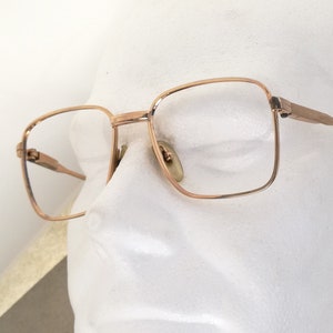 May include: Gold-tone metal eyeglasses with square lenses and black arms. The glasses are on a white mannequin head.