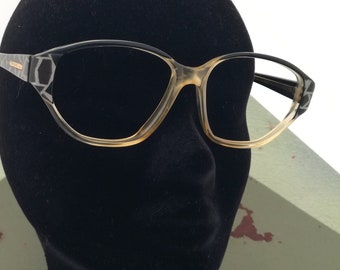 May include: Black and brown patterned eyeglasses with a clear frame and brown lenses. The eyeglasses are on a black mannequin head.