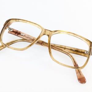 Peut inclure: Lunettes rectangulaires avec une monture translucide au motif écaille de tortue brun clair et beige. La branche intérieure porte l'inscription Apollo 44231/CA et le nombre 140 en blanc. Les montures ont une finition brillante et des verres clairs.
