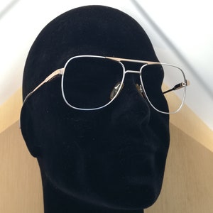 Peut inclure: Lunettes de vue de style aviateur argentées avec des accents dorés sur une tête de mannequin noire.