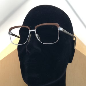 May include: A black mannequin head wearing a pair of silver and brown eyeglasses with a rectangular frame.