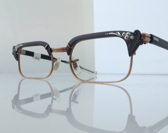May include: A pair of brown and gold spectacles with a decorative design on the arms. The glasses have a rectangular shape and clear lenses.