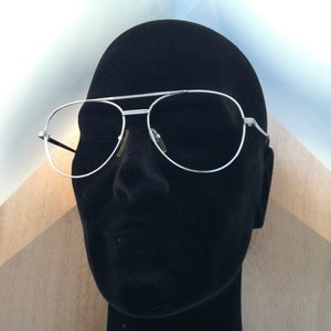May include: Silver aviator sunglasses with a black frame on a black mannequin head.