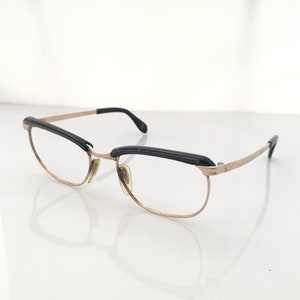 May include: Gold-tone metal spectacles with black plastic accents on the browline and temples.