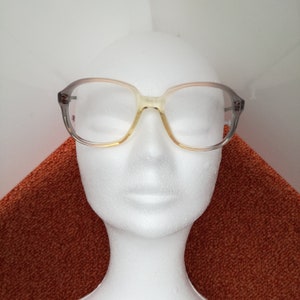 May include: A pair of eyeglasses with a light brown and gray frame. The frame has a rounded square shape with a slight cat-eye style. The lenses are clear.