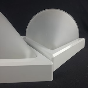 Może przedstawiać: Biała lampa w kształcie trójkąta z kloszem z matowego szkła. Lampa jest wykonana z tworzywa sztucznego i ma nowoczesny design.
