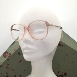May include: A pair of pink plastic framed eyeglasses with clear lenses. The glasses are on a white mannequin head.