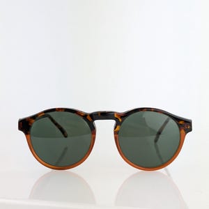 May include: Round sunglasses with a tortoiseshell pattern frame and dark green lenses. The sunglasses have a classic design with a brown and black frame. The lenses are a dark green color, providing a stylish and functional accessory.