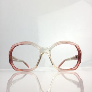 May include: A pair of pink plastic eyeglasses with a clear lens. The glasses have a rounded, oval shape and a thick frame.